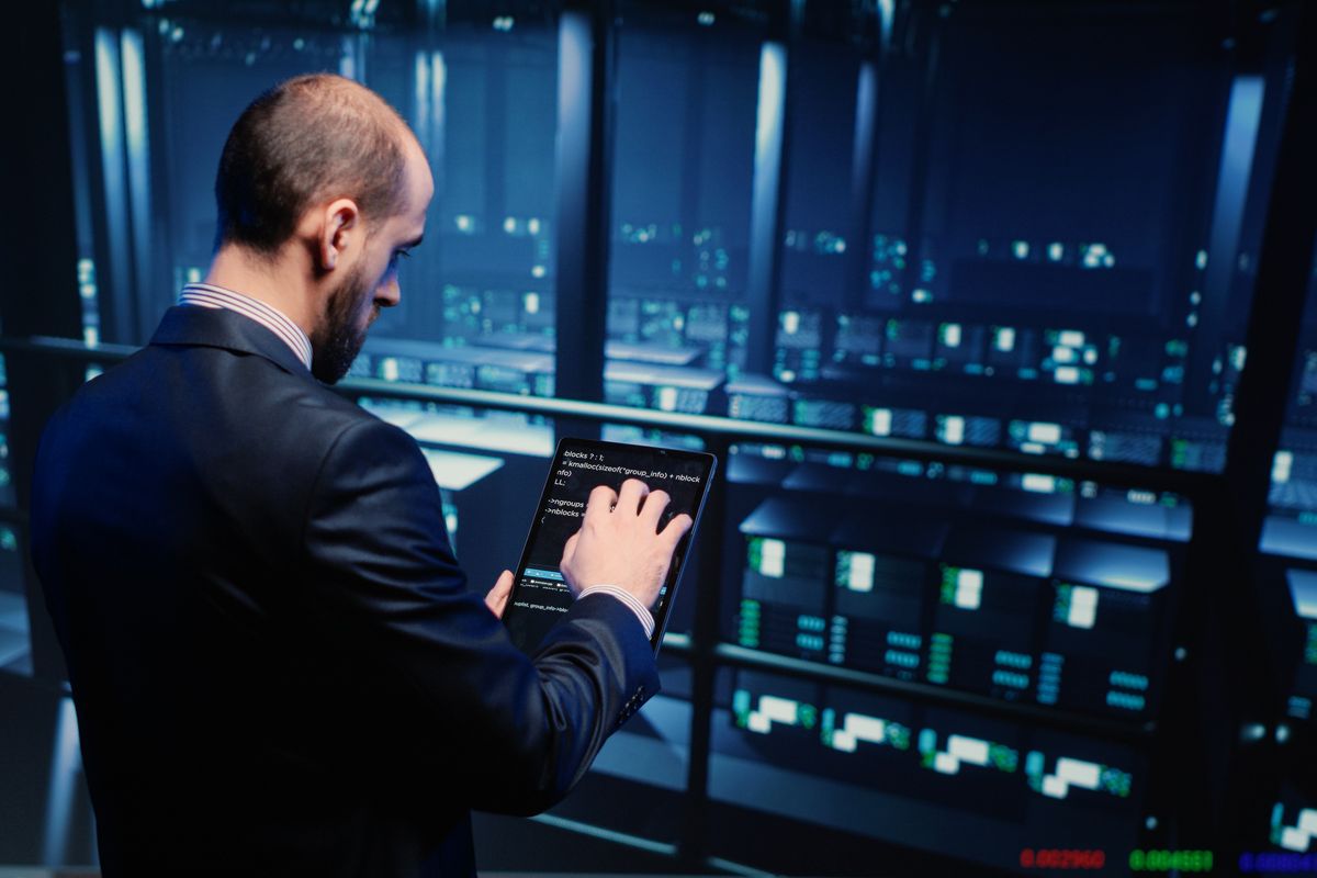 IT specialist in a dark suit using a tablet inside a server room, representing custom security software and IoT integration